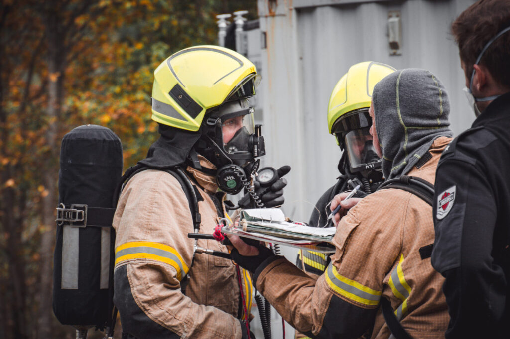 To røykdykkere snakker med røykdykkerleder. De ser hvor mye luft de har igjen etter innsats i røykfullt hus.