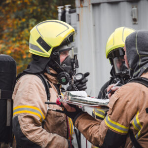 To røykdykkere snakker med røykdykkerleder. De ser hvor mye luft de har igjen etter innsats i røykfullt hus.